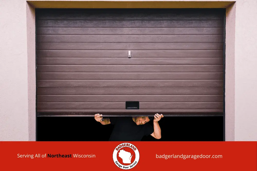 Why Garage Door Balance Matters More in Wisconsin Winters-1 A person peeks under a brown garage door, showcasing Garage Door Repair services in Wisconsin.| Badgerland Garage Door Service – Green Bay & Appleton Garage Door Repair