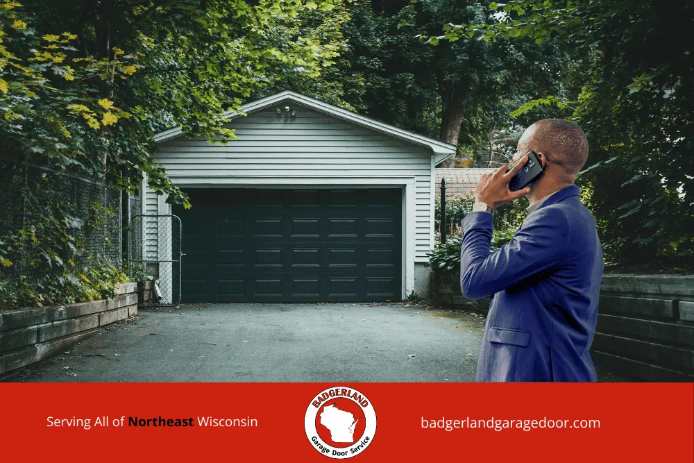 Why Garage Door Balance Matters More in Wisconsin Winters-3 A man in a blue suit talks on his phone in front of a closed garage door, possibly discussing Wisconsin garage door repair.| Badgerland Garage Door Service – Green Bay & Appleton Garage Door Repair