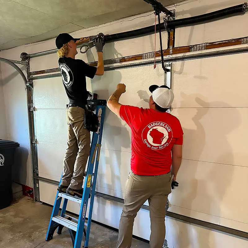 Two technicians in Badgerland shirts repairing a garage door in Appleton.| Badgerland Garage Door Service – Green Bay Garage Door Repair